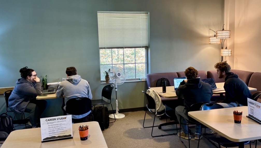 Two student advisors assisting two other students at small work tables in the Career Studio.